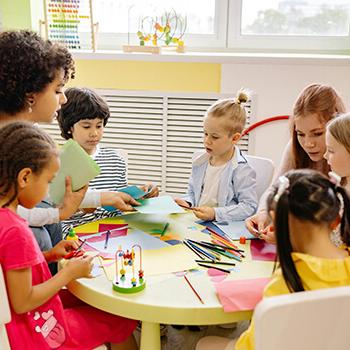 Student teachers work with children on a project around a table.